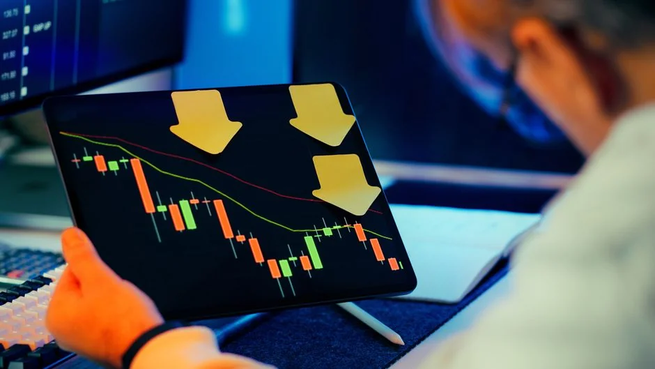 Two businessmen analyze stock market data using a smartphone and laptop in a modern office setting.